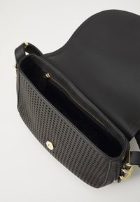 Zwarte schoudertas van perforated leer aan de voorkant, gouden hardware, ritszak en een gladde achterkant. Inclusief een verstelbare schouderriem.