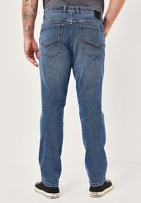Rückansicht von blauen Denim-Jeans mit geradem Schnitt, ausgestattet mit zwei Gesäßtaschen und Kontrastnähten. Getragen mit schwarzen Sneakern.