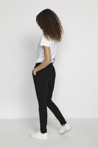 Sorte joggingbukser med elastisk talje, sidelommer, tapered ben og hvide sneakers, der er sat sammen med en kortærmet hvid T-shirt.