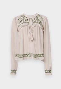 Blouse rose clair à manches longues avec des accents froncés, broderie florale verte sur le devant et l'ourlet, et un col noué avec un gland.