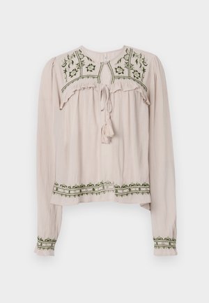 Ljusrosa långärmad blus med volanger, grön blomstermönstring på oket och fållen, samt en knytkrage med en tofs.