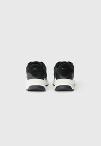 Sneakers atletici neri con suole bianche a contrasto, dotati di un materiale superiore liscio e branding discreto sul tallone. Stile imbottito.