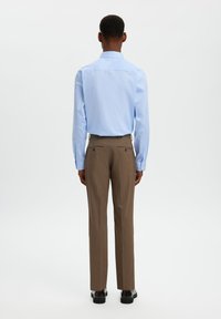 Ανοιχτό γαλάζιο πουκάμισο με μακριά μανίκια, πίσω όψη, σε συνδυασμό με καφέ παντελόνι ραμμένο κατά παραγγελία με δύο πίσω τσέπες και διακριτικές ραφές.