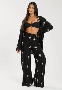 Conjunto negro compuesto por un top corto y pantalones de pierna ancha, con estampados de palmeras blancas. Tejido ligero con un corte relajado.