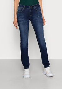 Donkerblauwe spijkerbroek met een slim fit, met voorzakken, riemlussen en subtiele vervaging. Gecombineerd met witte sportschoenen.