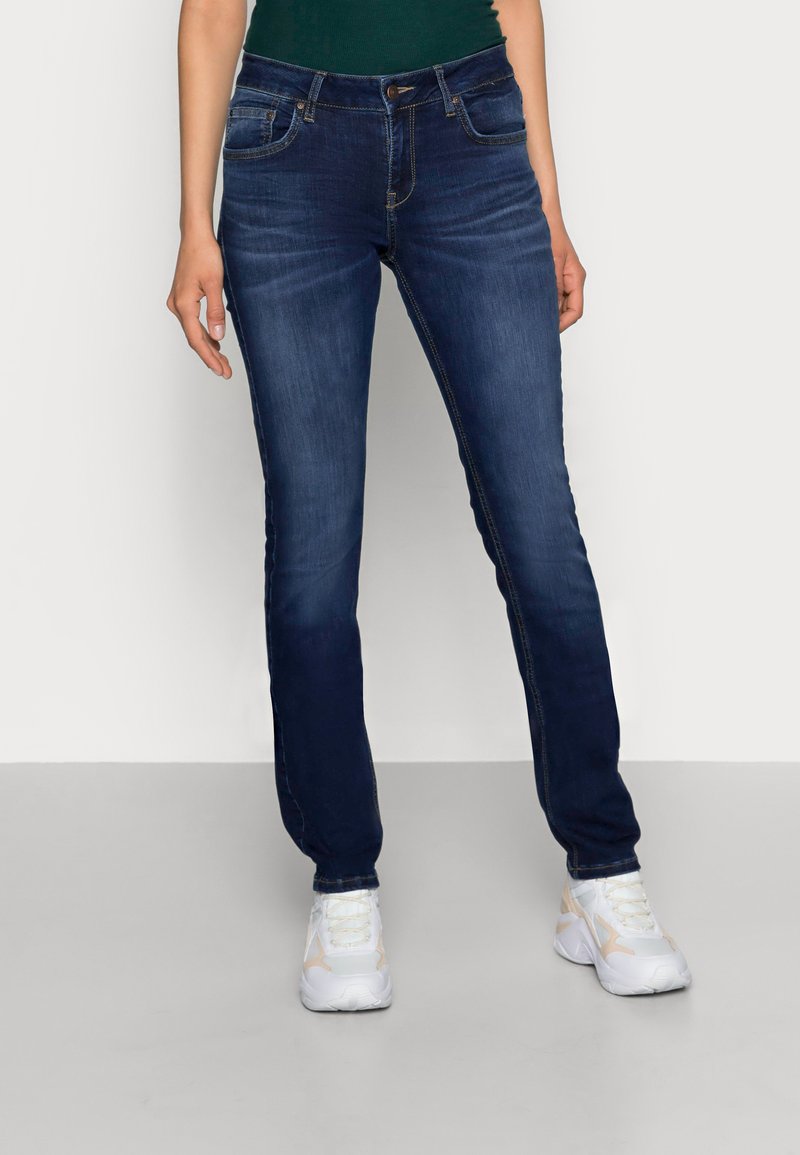 Donkerblauwe spijkerbroek met een slim fit, met voorzakken, riemlussen en subtiele vervaging. Gecombineerd met witte sportschoenen.
