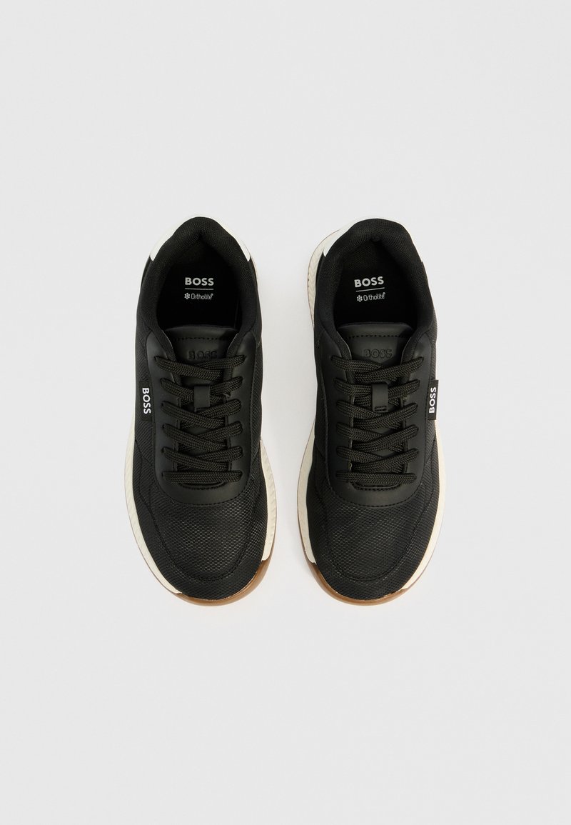 Une paire de baskets noires BOSS avec des semelles blanches, des lacets noirs et le logo BOSS sur la languette et le côté, présentée en vue de dessus sur fond blanc.