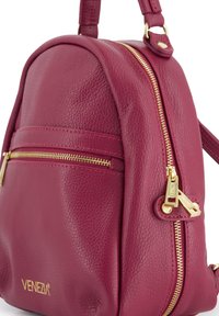 Bordeauxfarbener Leder-Rucksack mit runder Form, ausgestattet mit goldenen Reißverschlüssen und Akzenten, einem oberen Griff und einer vorderen Reißverschlusstasche.
