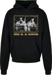 Sort hættebluse med en frontgrafik af to figurer inden for en guldindrammet design, med "ERIC B. & RAKIM" i fede bogstaver nedenfor.