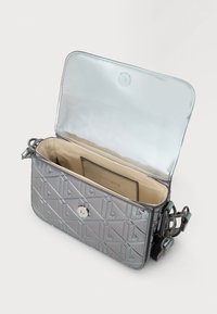 Klein metallic zilveren crossbody tas met reliëfpatroon, beige interieur, magnetische drukknoopsluiting en verstelbare riem met zichtbaar beslag.