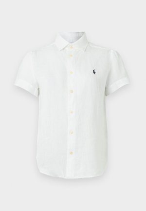 Λευκό πουκάμισο με κοντό μανίκι, κουμπιά και γιακά, με μικρό σκούρο λογότυπο στο αριστερό στήθος, εμφανιζόμενο σε απλό φωτεινό φόντο.