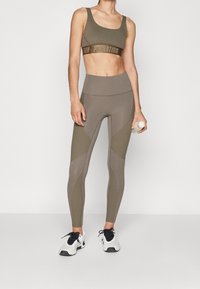 Top sportivo e leggings a vita alta in verde oliva smorzato, con un design testurizzato, pannelli a contrasto e una fascia con logo. Scarpe da ginnastica nere.