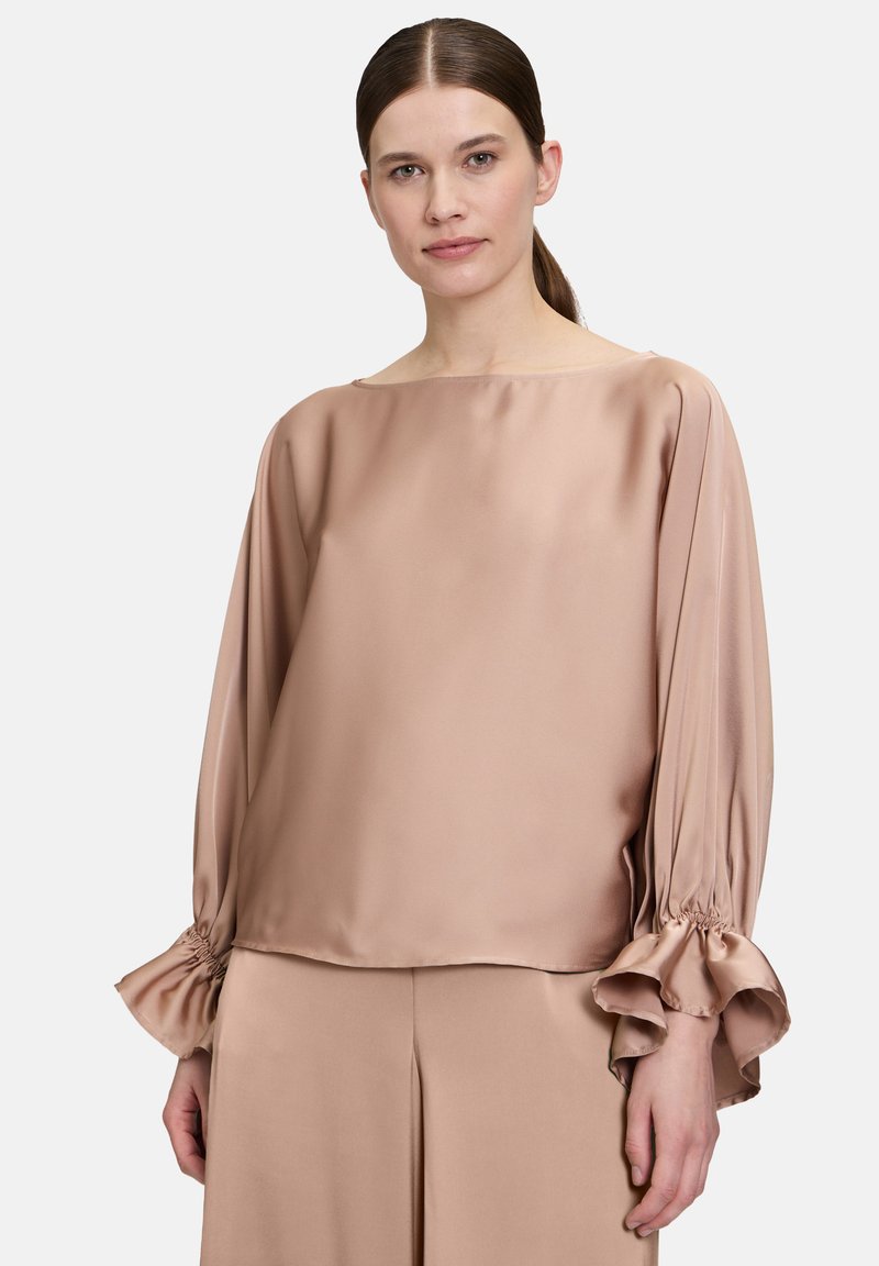 Blush-farbene Satinbluse mit weitem Ausschnitt, langen Ärmeln und gerafften Manschetten. Sanfte Textur und lockere Passform, kombiniert mit passender Hose.