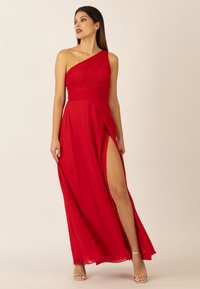 Rotes, einseitiges Kleid mit gefaltetem Oberteil, fließendem Rock und Oberschenkel-Spalte. Aus leichtem Stoff gefertigt, mit silbernen High Heels mit Knöchelriemen.