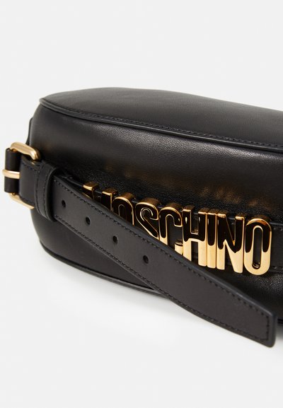 Geantă crossbody din piele neagră, cu un logo "Moschino" de culoare aurie, având o curea scurtă ajustabilă și o formă rotunjită. Detalii cu textură pe suprafață.