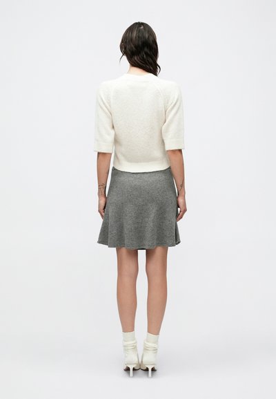 Ανοιχτό μπεζ πουλόβερ με κοντά μανίκια και υφή πλεκτού, συνδυασμένο με γκρι φαρδιά φούστα. Το μοντέλο φορά λευκά μποτάκια αστραγάλου με χαλαρό πλεκτό.