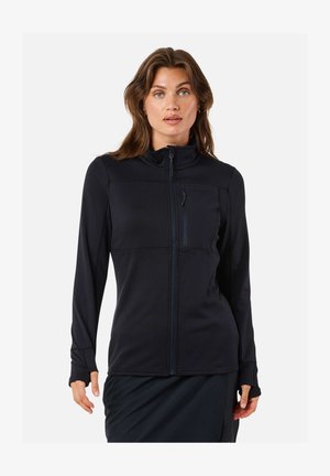 Žena so svetlou pokožkou a hnedými vlasmi, oblečená v čiernu bundu na zips s náprsným vreckom, stojaca na bielom pozadí.