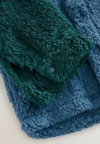 Gros plan sur un tissu en polaire texturé replié dans des couleurs turquoise et bleu, avec une surface douce et moelleuse.