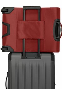 Valigia rossa in tessuto con manico estraibile posta sopra una valigia rigida grigia con texture scanalata e un manico laterale.