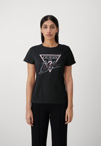Sort t-shirt med korte ærmer og en trekantet logo i pink og sølvfarvede paletter, med teksten "GUESS U.S.A." og en afslappet pasform.
