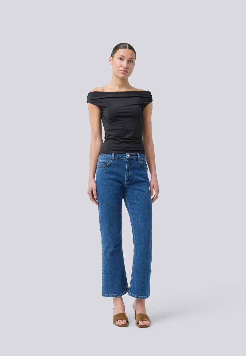 Zwarte off-shoulder top gecombineerd met rechte spijkerjeans in blauw. Model draagt bruine slide sandalen. Eenvoudig en aansluitend ontwerp.