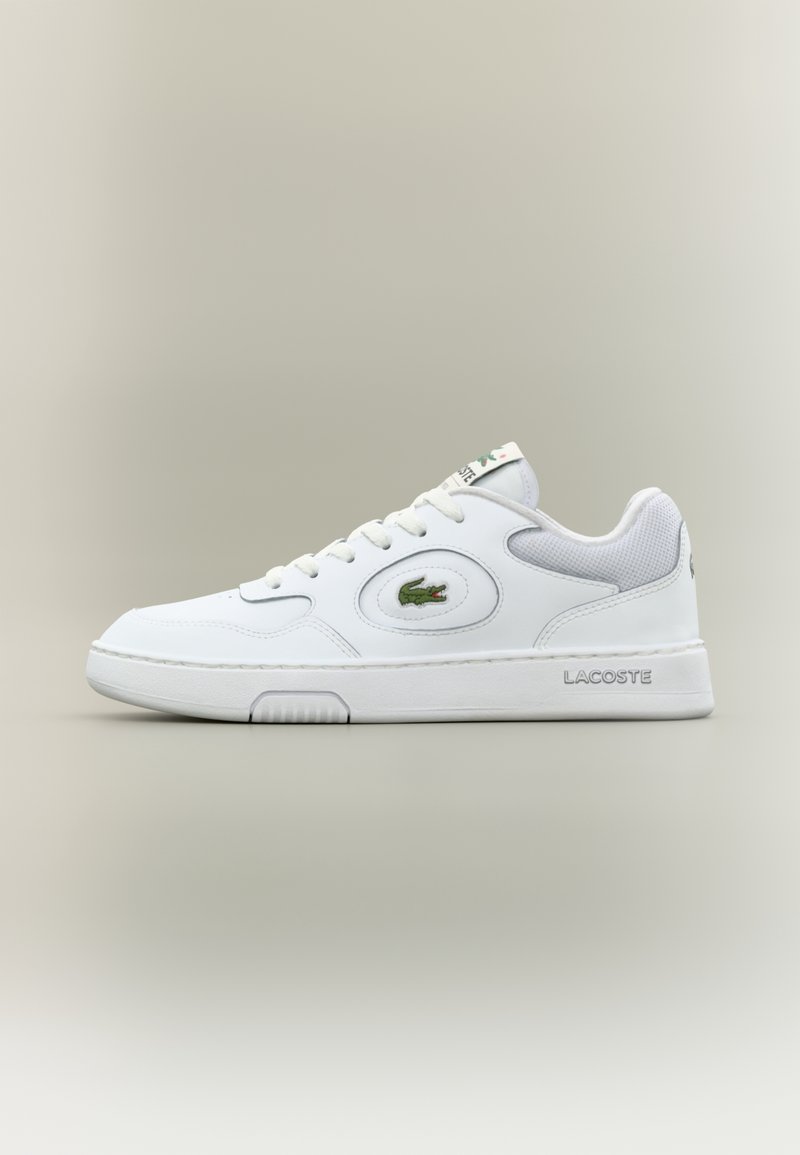Baskets blanches avec tige en cuir lisse, semelle en caoutchouc, bout arrondi, et accents en mesh. Présente un logo Lacoste vert et un talon texturé.