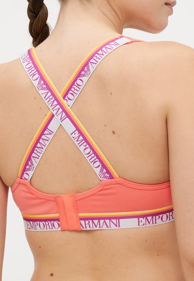 Coral sports bra with X-back straps. Features white, pink, and yellow branded elastic bands. Smooth texture and fitted design.