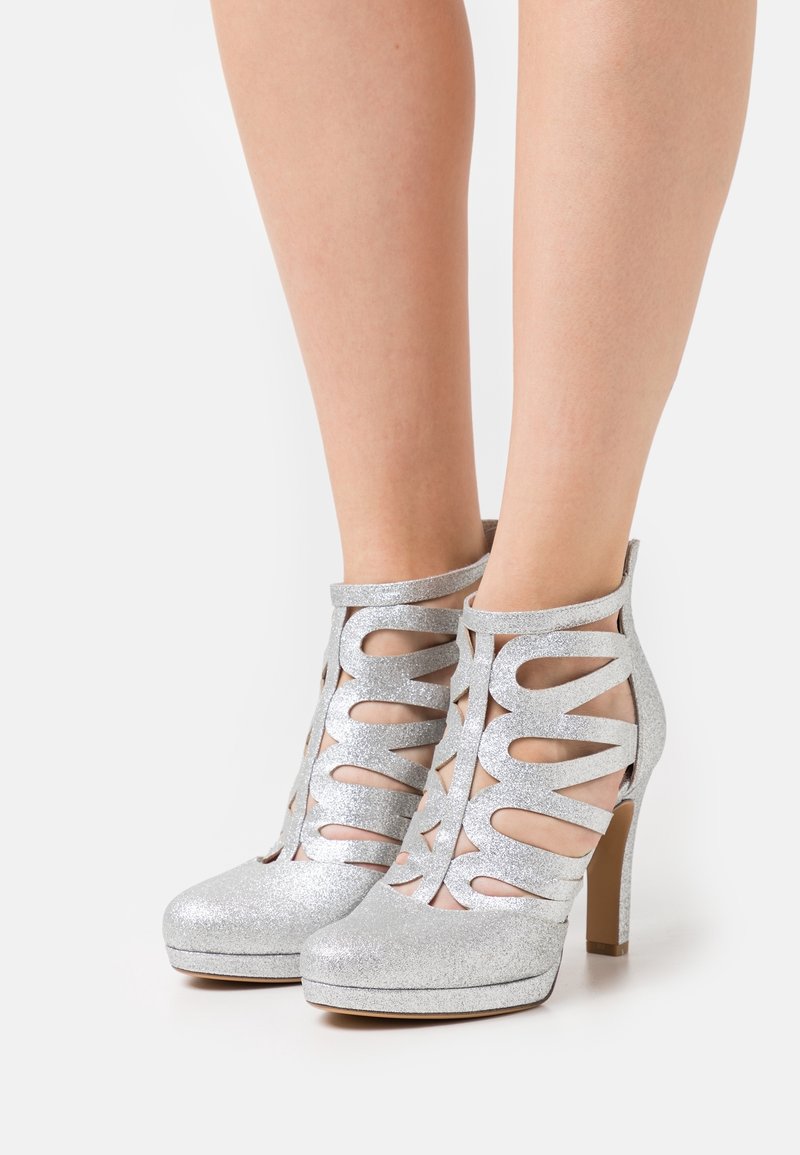 Bottes argentées à paillettes avec design ajouré, talon haut, bout arrondi et surface texturée. Présentent plusieurs fentes pour un style supplémentaire.