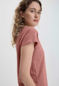Camiseta de manga corta y cuello redondo en color rosa empolvado, fabricada con tela suave, con un corte relajado y detalles de costura visibles.