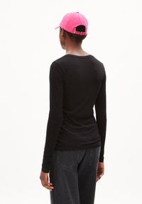 Schwarzes Langarmshirt mit Rundhalsausschnitt, kombiniert mit einer leuchtend pinken Baseballmütze, die eine glatte Textur und eine lässige Passform zeigt.