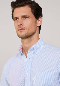 Camicia di cotone a righe blu chiaro e bianche con colletto abbottonato, taschino sul petto e un sottile accento rosa all'interno del colletto.