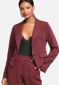Burgundský oblekový blazer z hladké tkaniny, s výstřihovým límcem, dvěma kapsami a zapínáním na jeden knoflík, v kombinaci s černým krajkovým body.