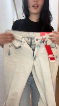 Femme portant une chemise noire tenant un jean de couleur claire avec une étiquette rouge de la marque Diesel dans un environnement intérieur.