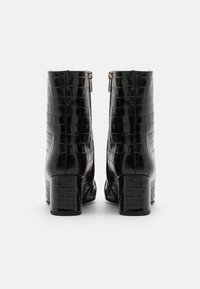 Botines negros con textura de cocodrilo brillante, tacones gruesos y cremalleras en tono dorado en la parte trasera. Diseño simple y elegante.