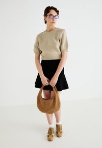 Beige kötött crop pulóver, fekete harangszoknya, barna fonott válltáska, világosbarna sneaker fehér részletekkel és fehér bokazokni.
