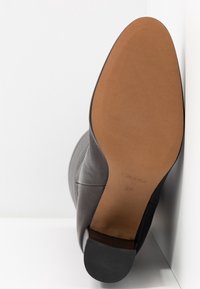 Sort læderankelstøvle med en glat overdel, rund tå og tanfarvet gummisål. Hælen er let forhøjet og har en mat finish.