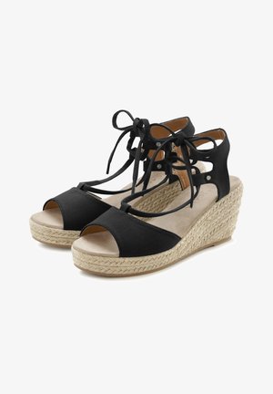Black wedge sandals with a woven jute sole, open toe design, crisscrossing black fabric straps, and adjustable lace-up accents.