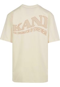 Cream-colored T-shirt made of soft cotton, featuring a large graphic print with "KANDI" and "THE ORIGINATOR OF STREETWEAR" in light brown.