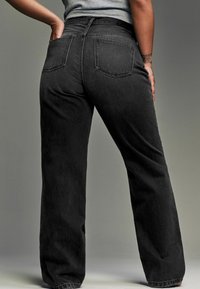 Los pantalones de mezclilla negros de pierna ancha cuentan con una cintura alta, cinco bolsillos y un acabado texturizado, con costuras visibles a lo largo de las costuras.