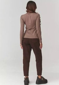 Brązowa bluzka z długim rękawem w połączeniu z ciemnobrązowymi spodniami i masywnymi czarnymi butami. Strój prezentuje prosty fason i gładką teksturę.