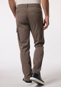 Hnědé cargo kalhoty s bočními kapsami, zapínacími zadními kapsami a rovnými nohavicemi. Nošeny s námořnickými teniskami. Hladká, odolná tkanina.