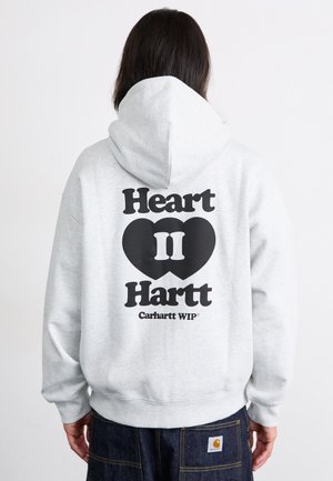 Grå hettegenser med stor svart tekst "Heart II Hartt" og hjertegrafikk på baksiden, med avslappet passform og ribbede mansjetter.