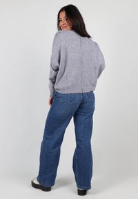 Pull en tricot gris avec un col rond, des épaules tombantes et une couture centrale. Associé à un jean en denim bleu taille haute à jambes évasées et des chaussures noires.