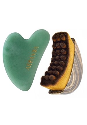 Pierre gua sha verte en forme de cœur avec le mot "AREANNA" en or à côté d'une brosse faciale à manche en bois avec des poils foncés.