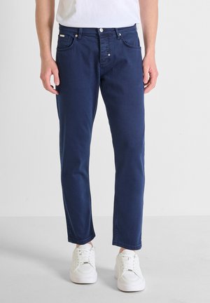 Jeans de mezclilla azul marino con corte recto, cinco bolsillos y sutilezas en los detalles de costura. Llevados con zapatillas blancas para crear contraste.