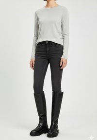 Haut à manches longues gris clair, jean slim fit gris foncé et bottes en cuir noires hautes avec semelles texturées et design montant jusqu'au genou.
