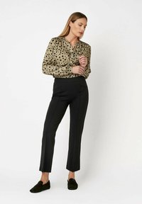 Beżowa bluzka w czarne kropki, z długimi rękawami i marszczonymi ramionami; zestawiona z dopasowanymi czarnymi spodniami i ciemnymi butami wsuwanymi.