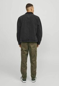 Schwarze Denimjacke mit geripptem Kragen, lockere Passform, kombiniert mit olivgrünen Cargo-Hosen mit seitlichen Taschen und hochgekrempelten Säumen.