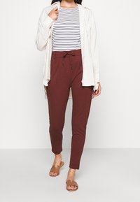 Maroon tapered pants with an adjustable drawstring waist, paired with a white button-up shirt and striped top. Brown slide sandals.