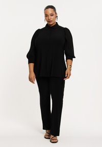 Schwarze Bluse mit Knöpfen und Puffärmeln, kombiniert mit schwarzen geraden Hosen. Glattes Material, minimalistisches Design mit subtilen Details.
